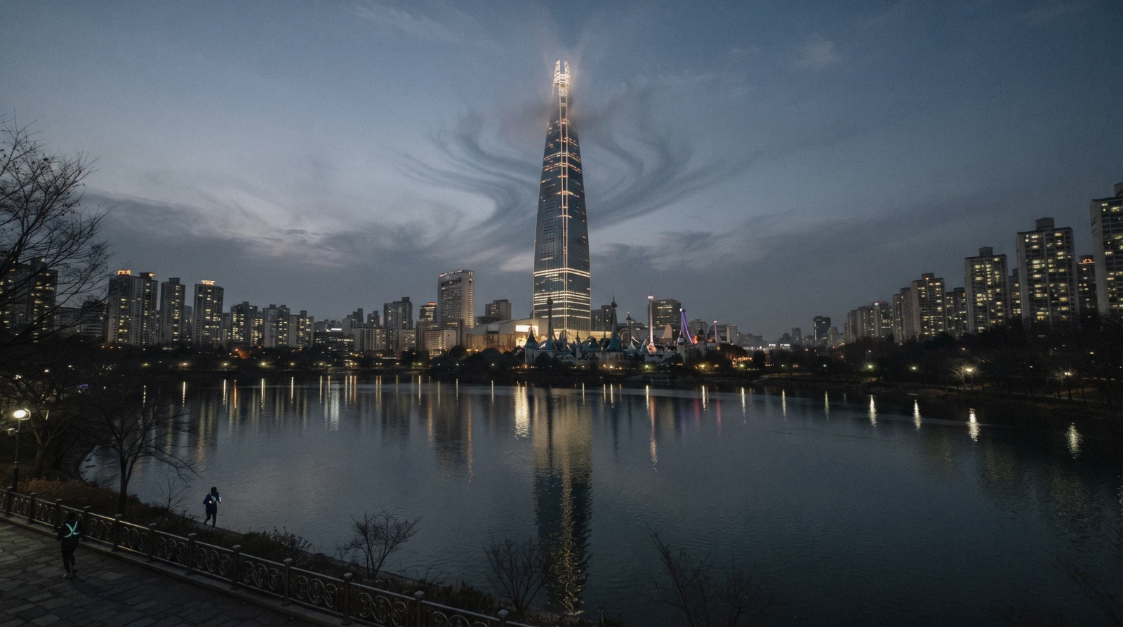 Lotte World Tower tapering into cloud above Jamsil reflected in Seokchon Lake, Seoul, South Korea